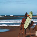 a man and woman on camel with surfboard on beach