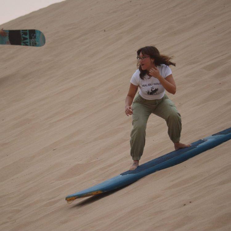 Tourists sandboarding down golden dunes during Timlalin Sandboarding Experience near Agadir